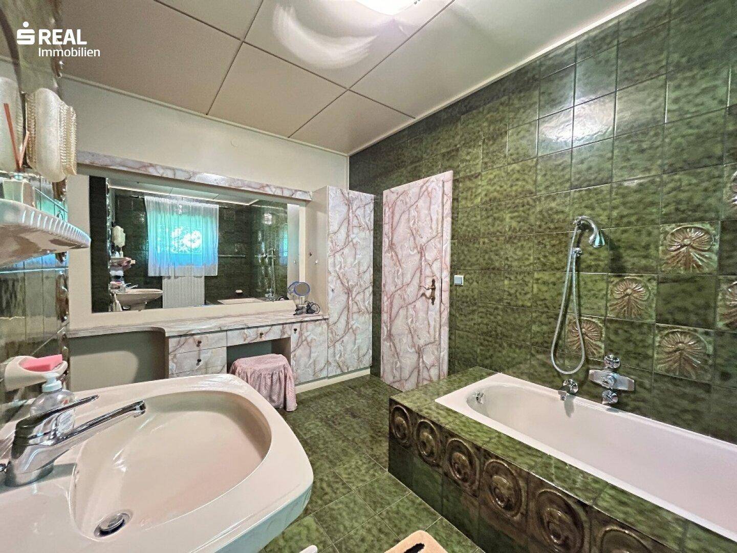 Geräumiges Badezimmer mit grünen Fliesen, Badewanne und einem Waschtisch mit großem Spiegel.