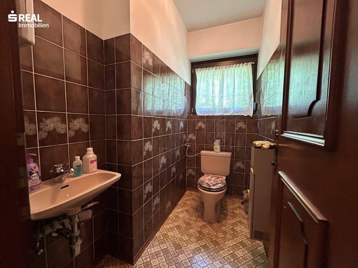 Kleines Gäste-WC mit braun-weißen Fliesen, Toilette, Waschbecken und Fenster.