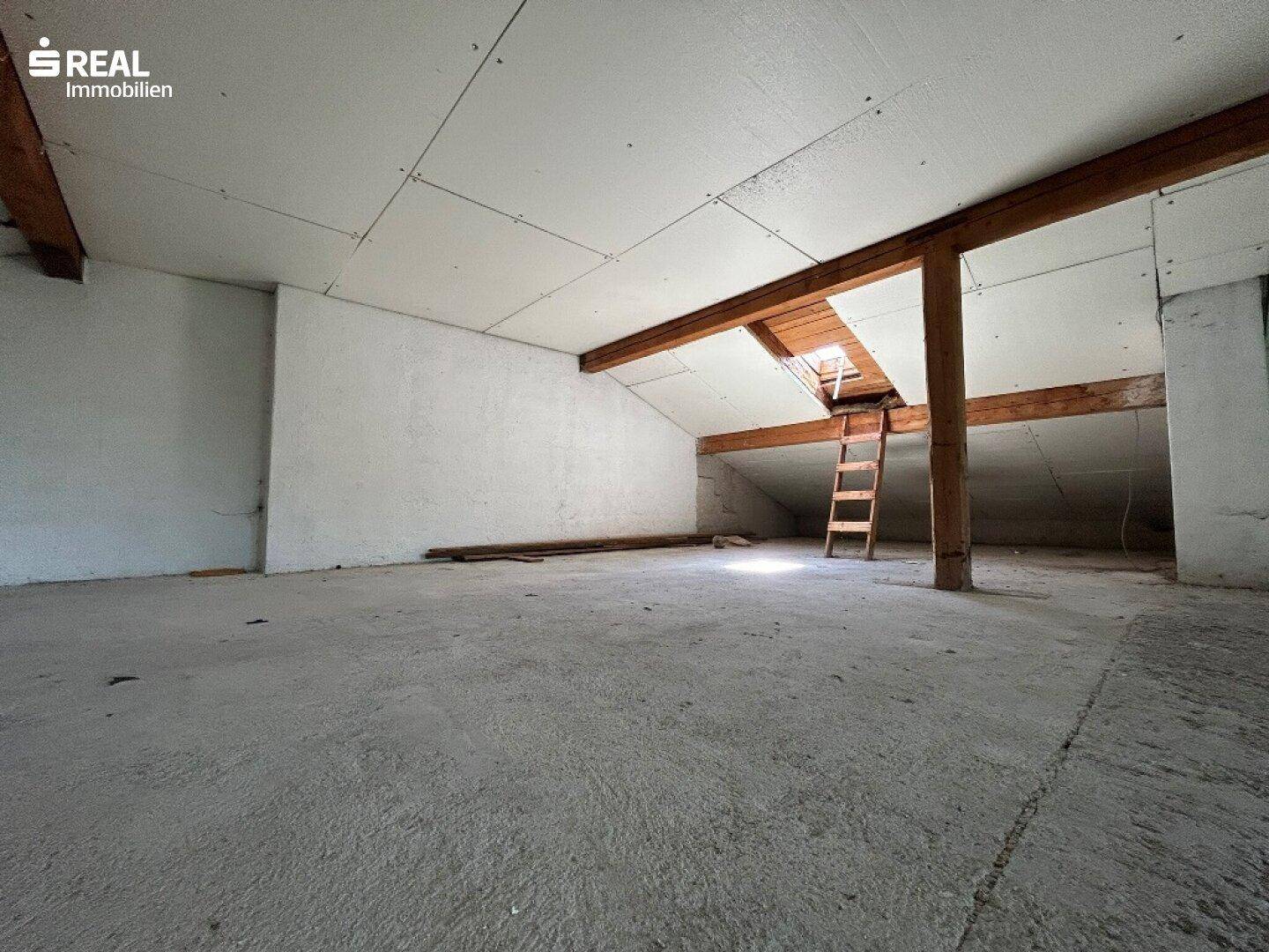 Unausgebauter Dachboden mit sichtbaren Holzbalken und Betonboden, bereit für den Ausbau.