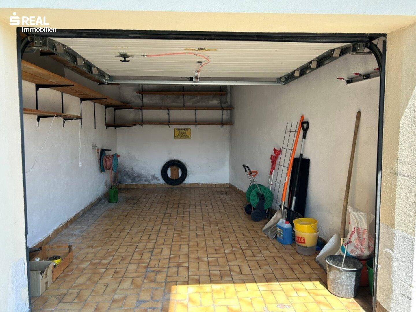 Geräumige Garage mit Fliesenboden, Regalen und Platz für Werkzeuge und Fahrzeuge.