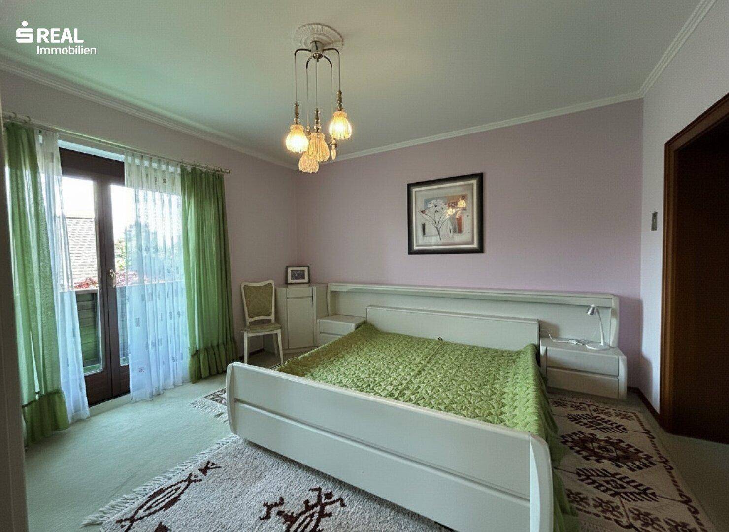 Helles Schlafzimmer mit weißem Bett, Teppichboden und direktem Zugang zu einem Balkon.