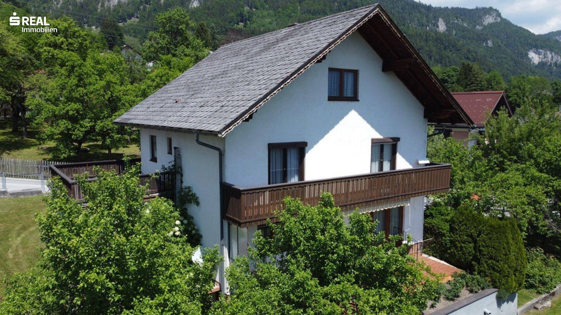 Ansicht des Einfamilienhauses von der Seite mit Satteldach und Balkon, eingebettet in eine grüne Landschaft.