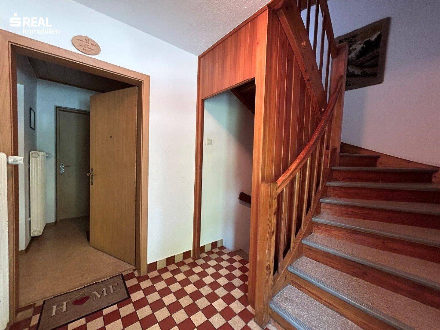 Eingangsbereich mit Holztreppe und kariertem Fliesenboden, der zu den oberen Etagen führt.