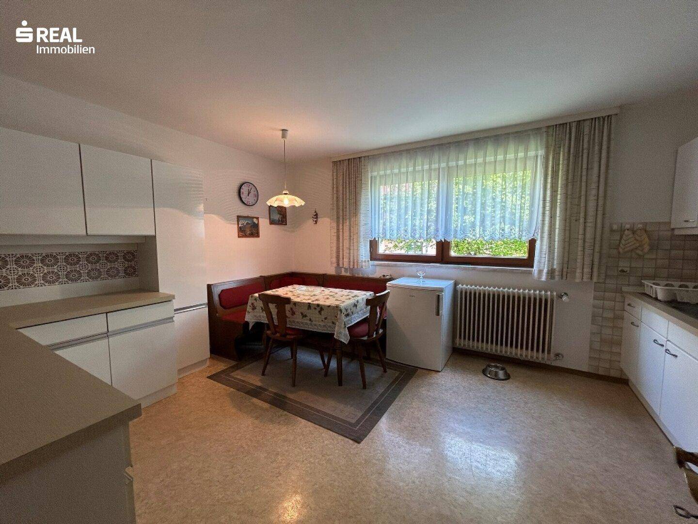 Geräumige Küche mit Essbereich, weißen Schränken und einem Fenster mit Blick ins Grüne.