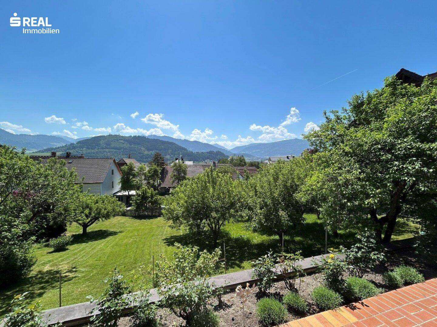 Panoramablick über die grüne Landschaft und die umliegenden Berge unter einem klaren blauen Himmel.
