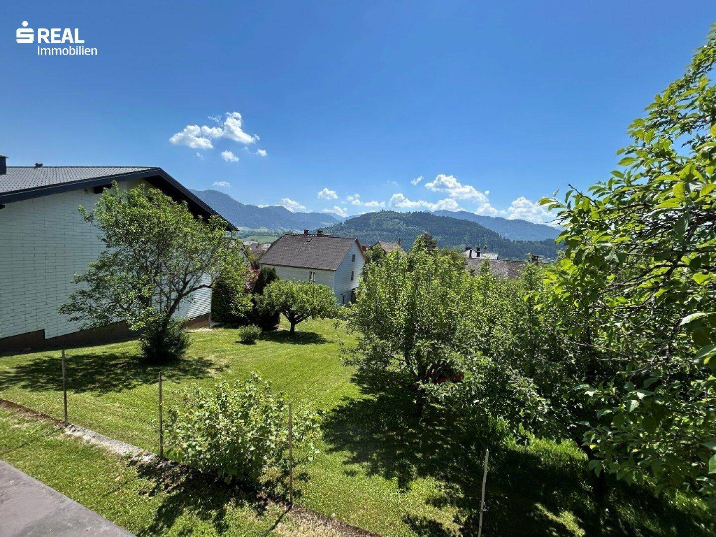 Großer, gepflegter Garten mit Rasenfläche und Obstbäumen, bietet einen weiten Blick auf die umliegende Berglandschaft.