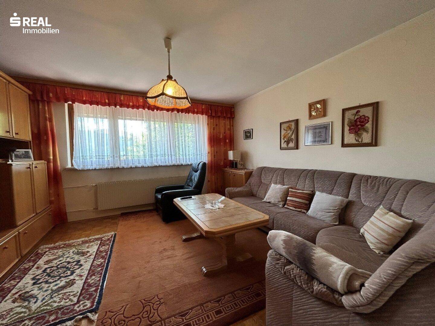 Gemütliches Wohnzimmer mit Sofa, Couchtisch und Fenster, das viel Tageslicht hereinlässt.