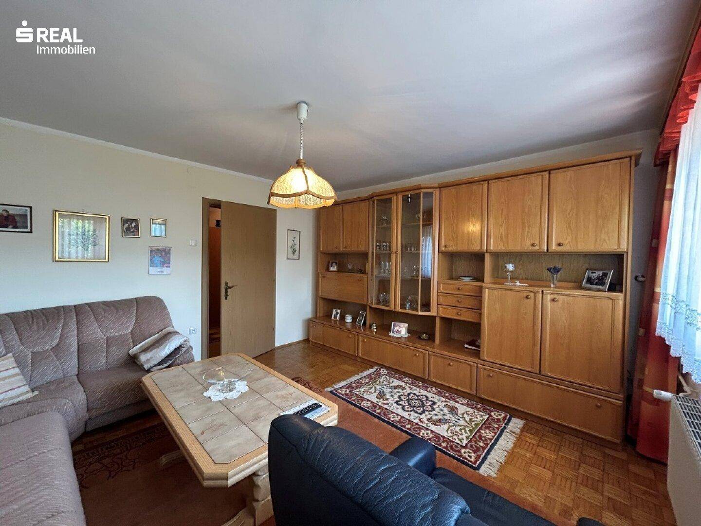 Wohnzimmer mit großer Holzschrankwand, Sofa und Parkettboden, bietet viel Stauraum.