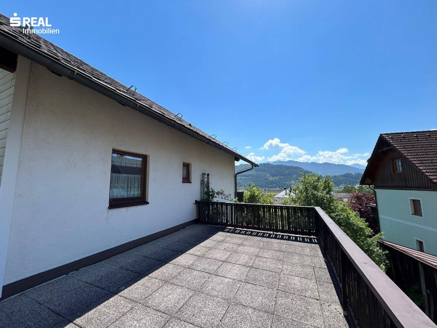 Großer Balkon mit Fliesenboden und Holzgeländer, bietet einen weiten Blick auf die Umgebung.