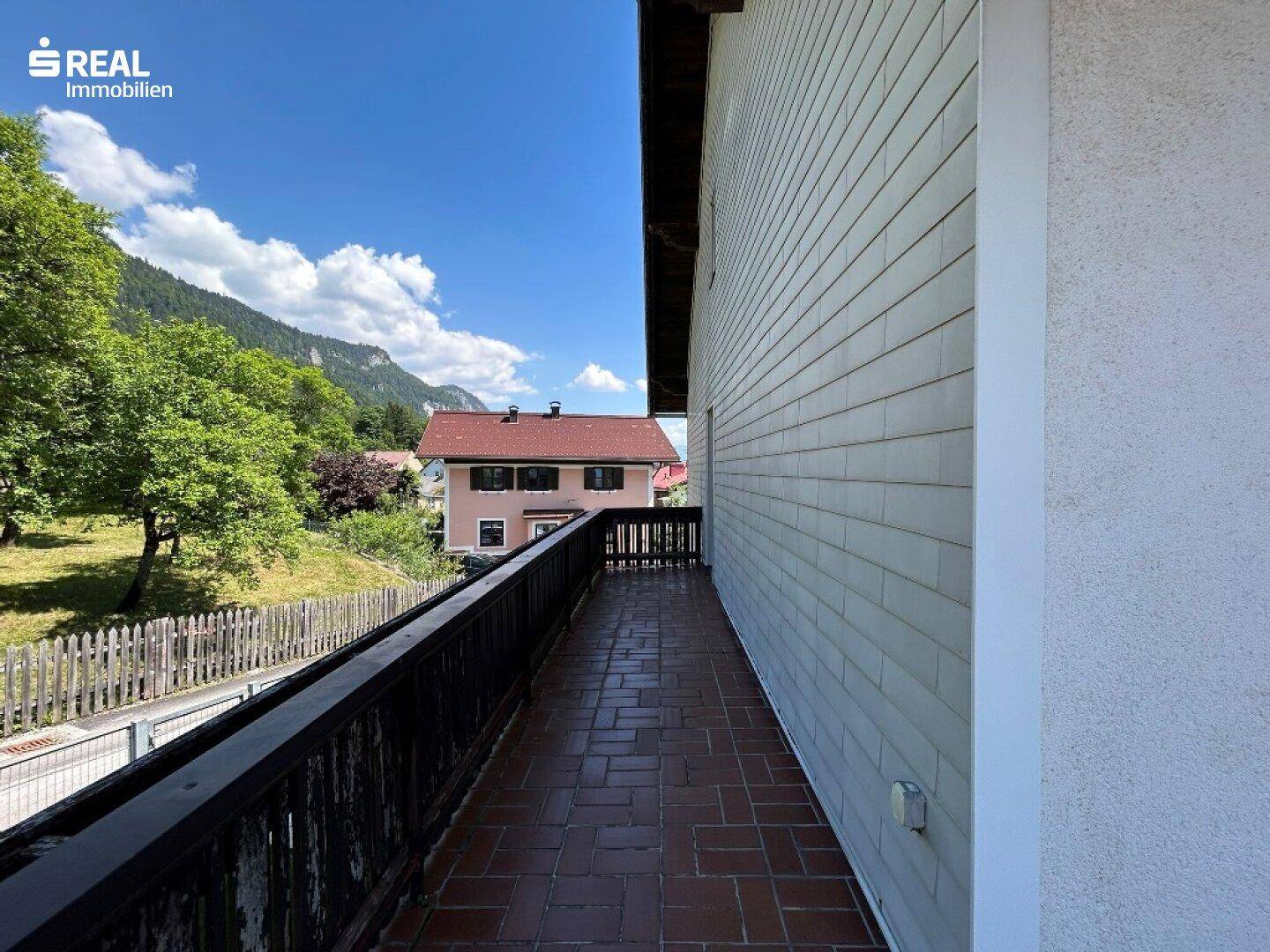 Langer Balkon mit Ziegelboden und Blick auf die umliegende Landschaft und Berge.