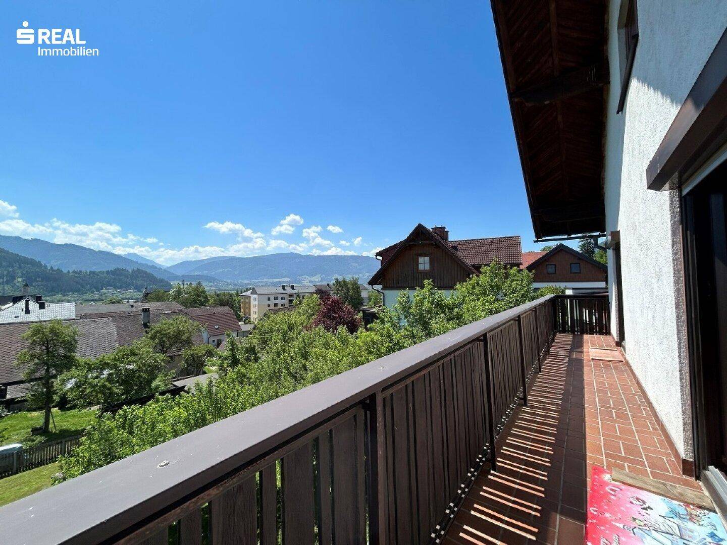 Balkon mit Holzbalkonbrüstung und weitem Blick über die Dächer und Berge.