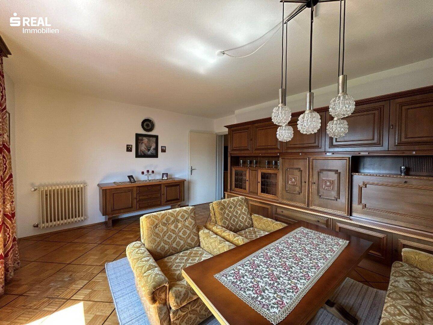 Wohnzimmer mit traditionellen Holzmöbeln, Parkettboden und einer dekorativen Deckenleuchte.