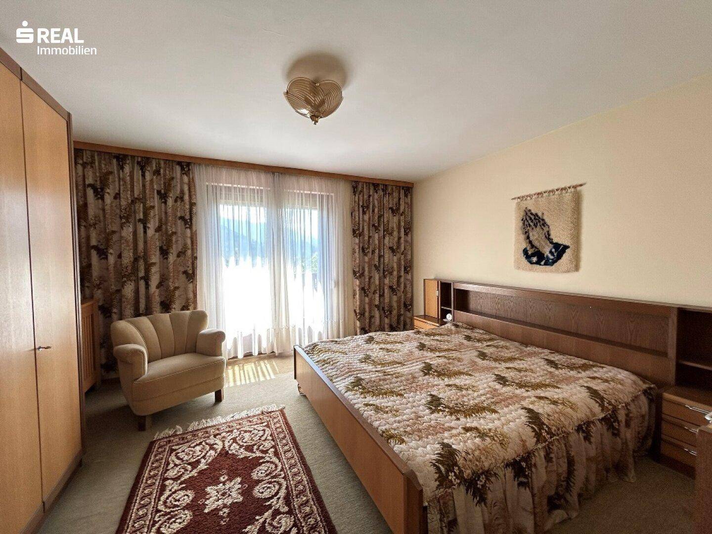 Schlafzimmer mit großem Doppelbett, Teppichboden und Zugang zu einem Balkon oder Fenster.