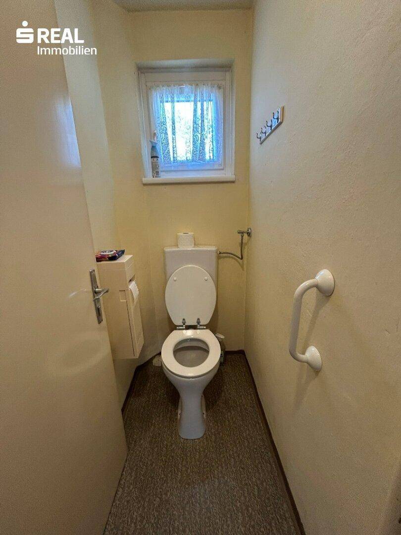 Separate Toilette mit Fenster, hellen Wänden und Haltegriff für zusätzliche Sicherheit.