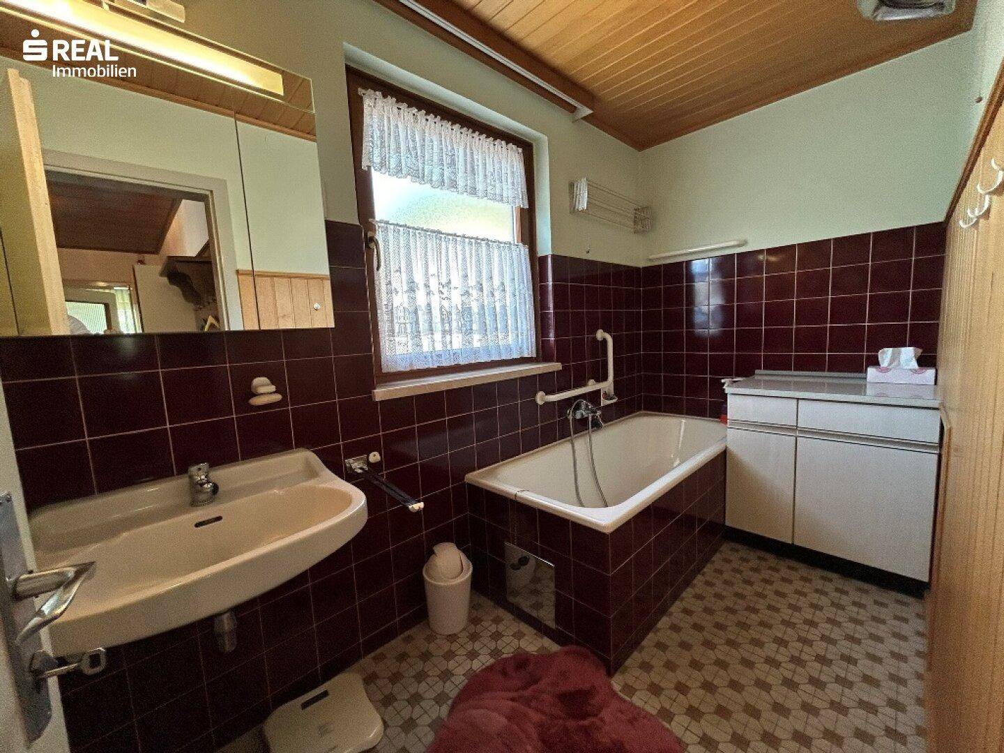 Badezimmer im 80er-Jahre-Stil mit burgunderroten Fliesen, Badewanne und Fenster.