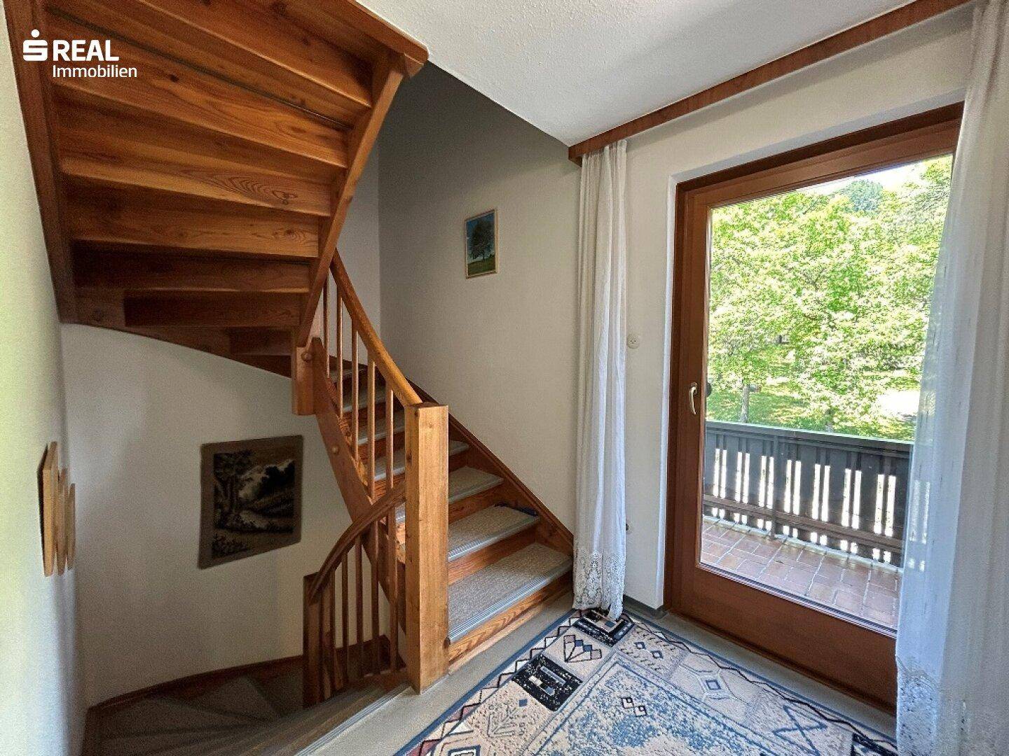 Holztreppe führt zu den oberen Etagen, mit Zugang zu einem Balkon oder einer Terrasse.