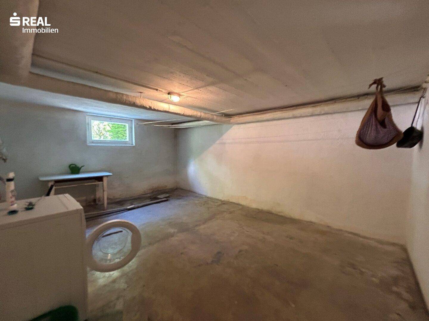 Geräumiger Kellerraum mit Waschmaschine, kleinem Fenster und Betonboden.