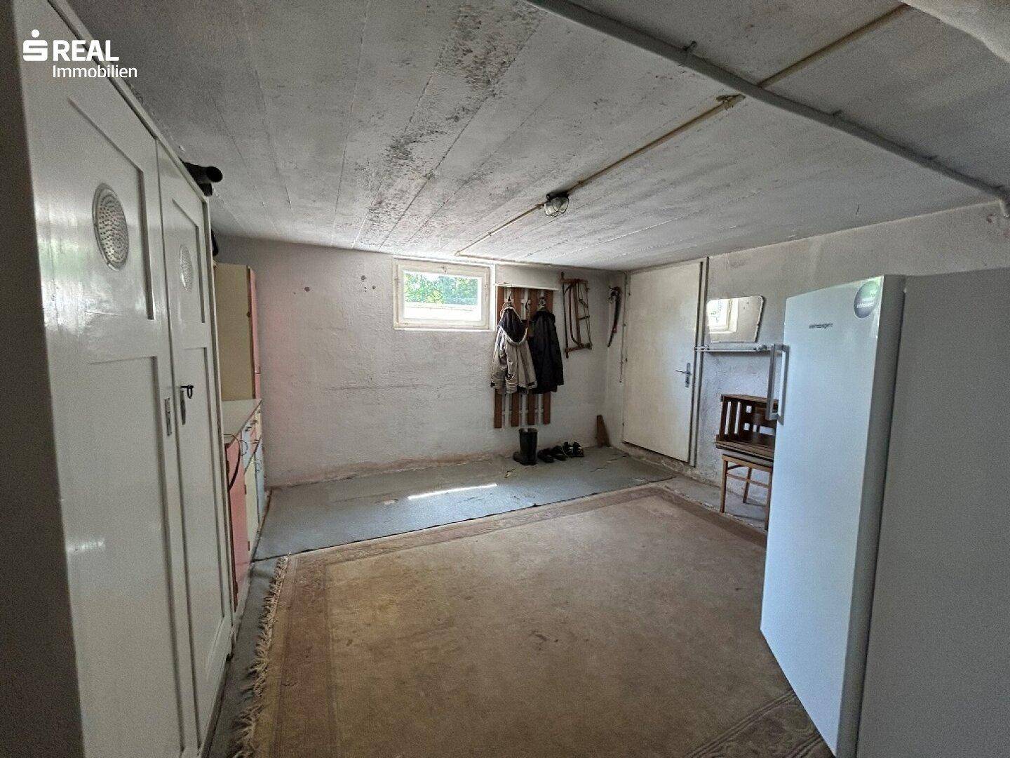 Kellerraum mit Kühlschrank, Fenster und Stauraum, ideal für Vorräte oder Hobby.