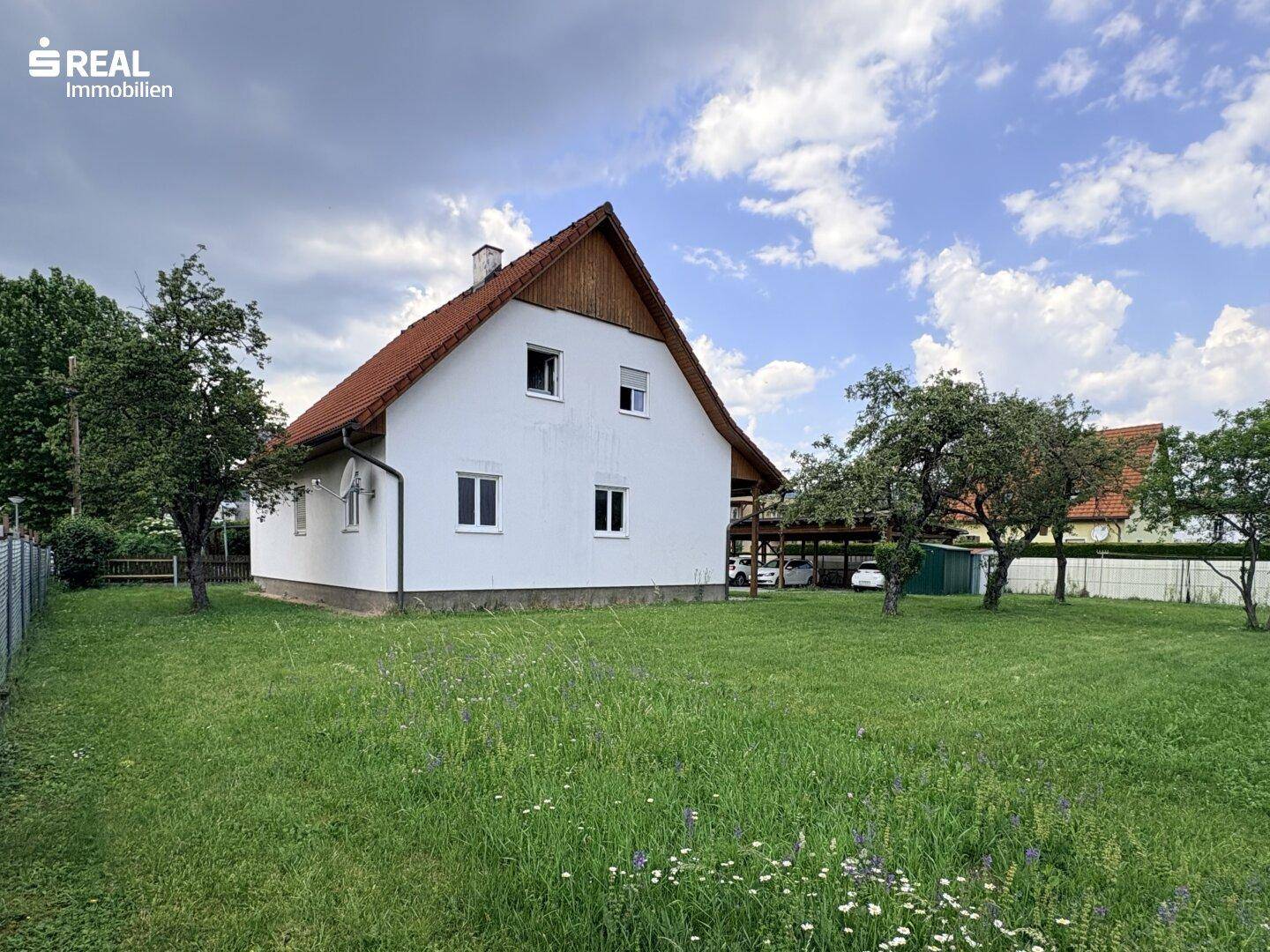 Rückansicht des Einfamilienhauses mit weitläufigem Garten und Obstbäumen an einem sonnigen Tag.