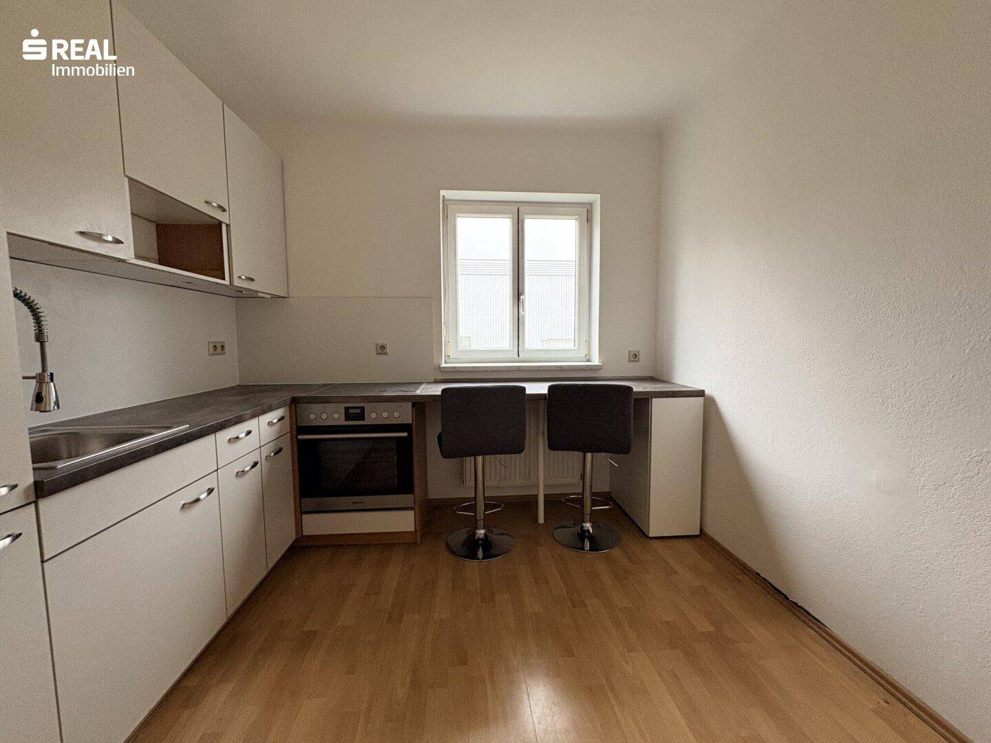 Helle Küche mit weißen Schränken, integriertem Backofen und einer Frühstücksbar am Fenster.
