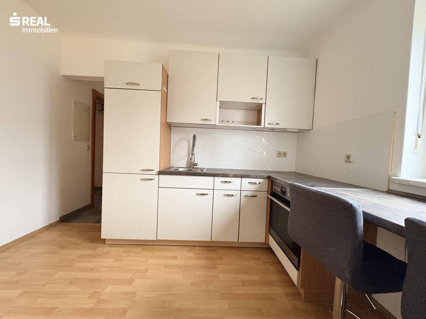 Funktionale Küche mit weißen Oberschränken, Spüle und Kühlschrank in einem hellen Raum.