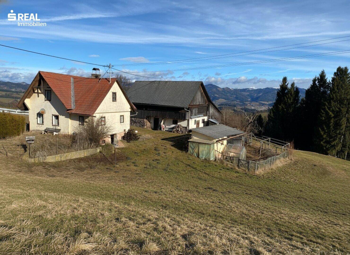 Zwei ländliche Gebäude auf einem Hügel mit weitem Blick auf die umliegende Landschaft und Berge.
