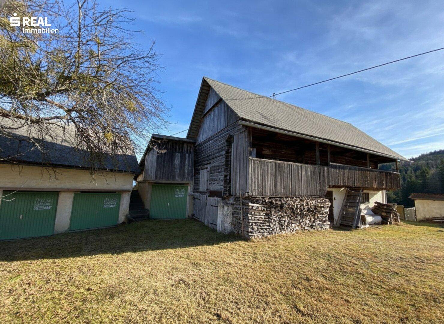 Rustikales Holzhaus mit Balkon und Holzstapel, umgeben von ländlicher Natur und Bergen.