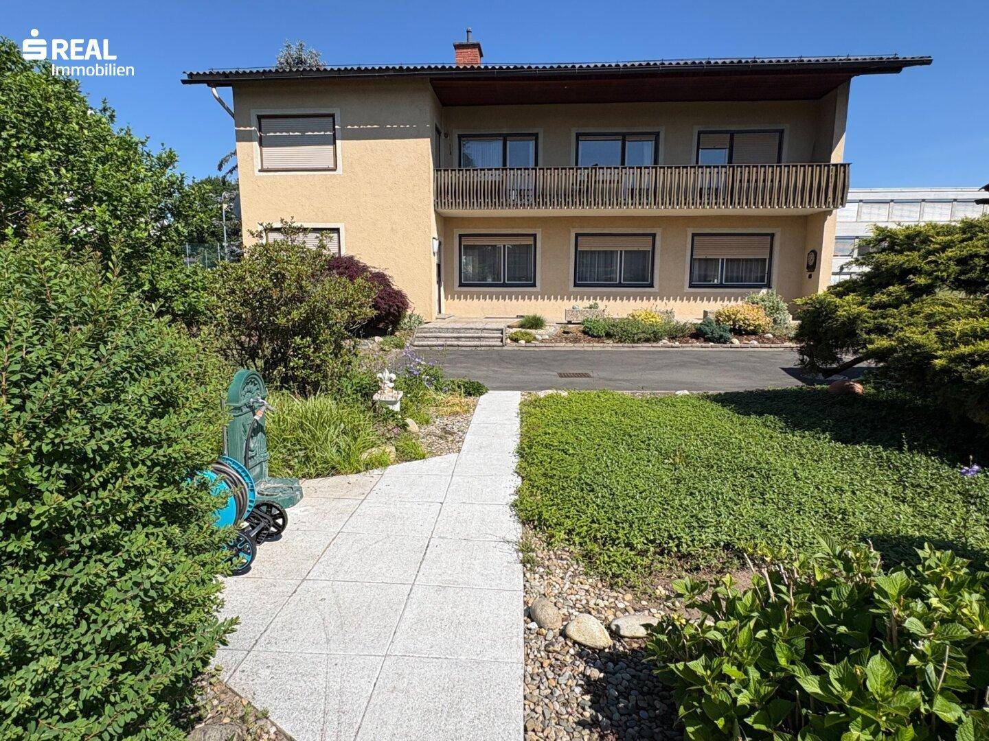 Zweistöckiges Wohnhaus mit mehreren Balkonen, umgeben von einem gepflegten Vorgarten und Auffahrt.