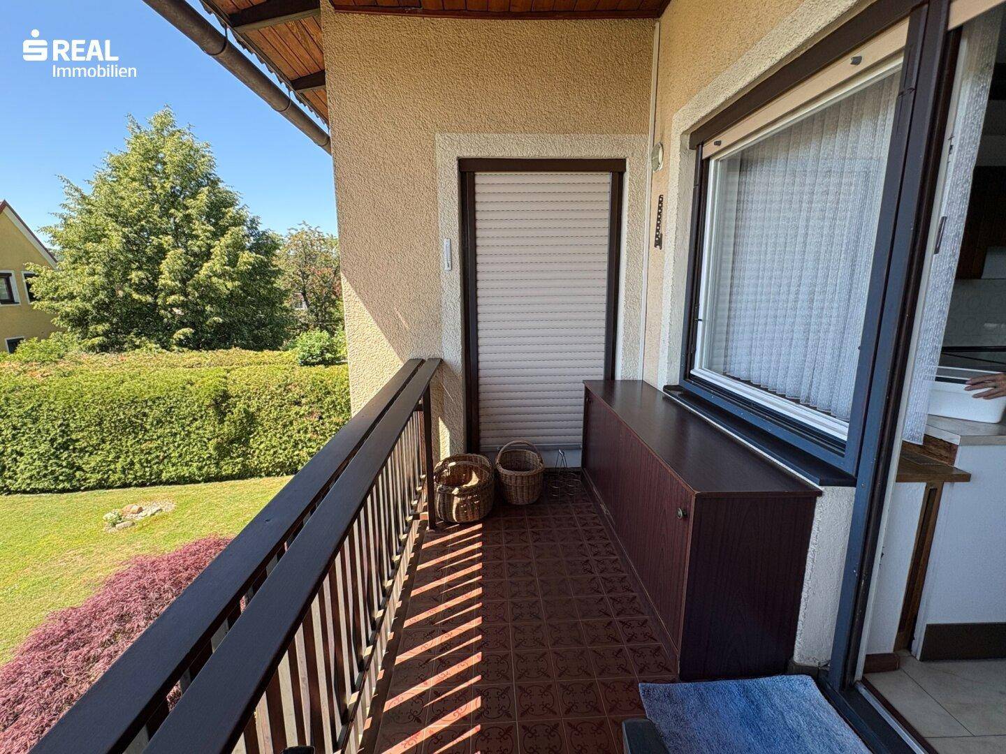 Sonniger Balkon mit Fliesenboden, Holzgeländer und Blick auf den grünen Gartenbereich.