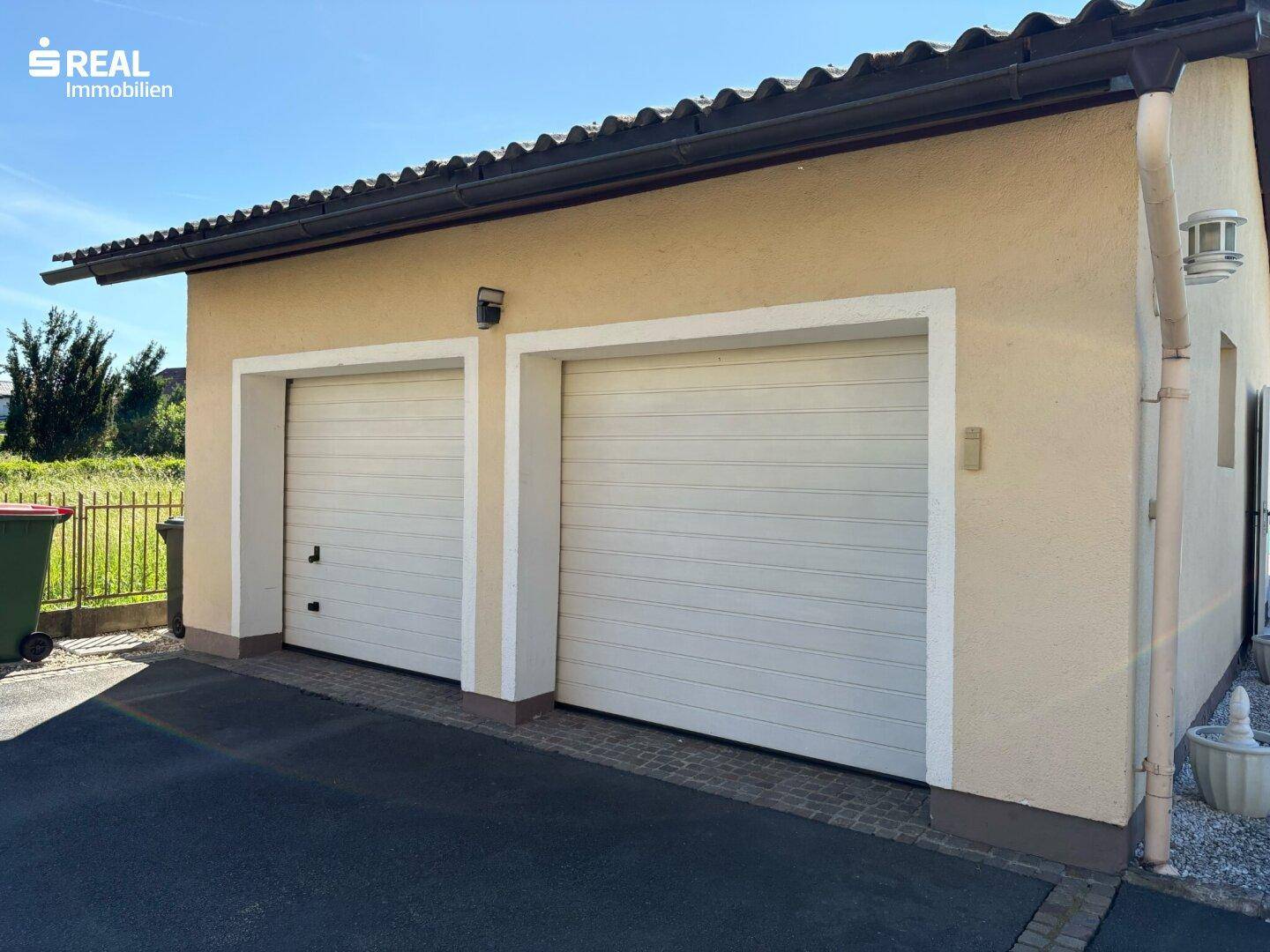 Doppelgarage mit zwei weißen Toren und einer gepflasterten Zufahrt unter blauem Himmel.