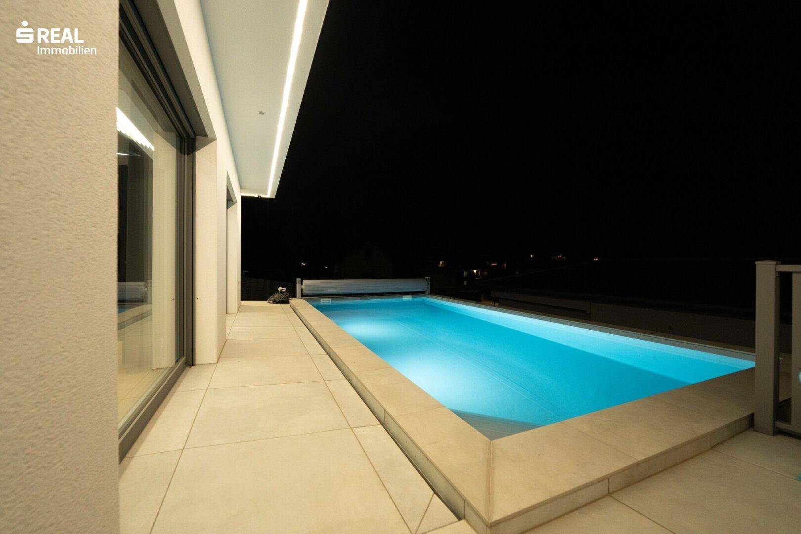 Außenbereich der Villa bei Nacht mit beleuchtetem Pool und umliegender Terrasse.
