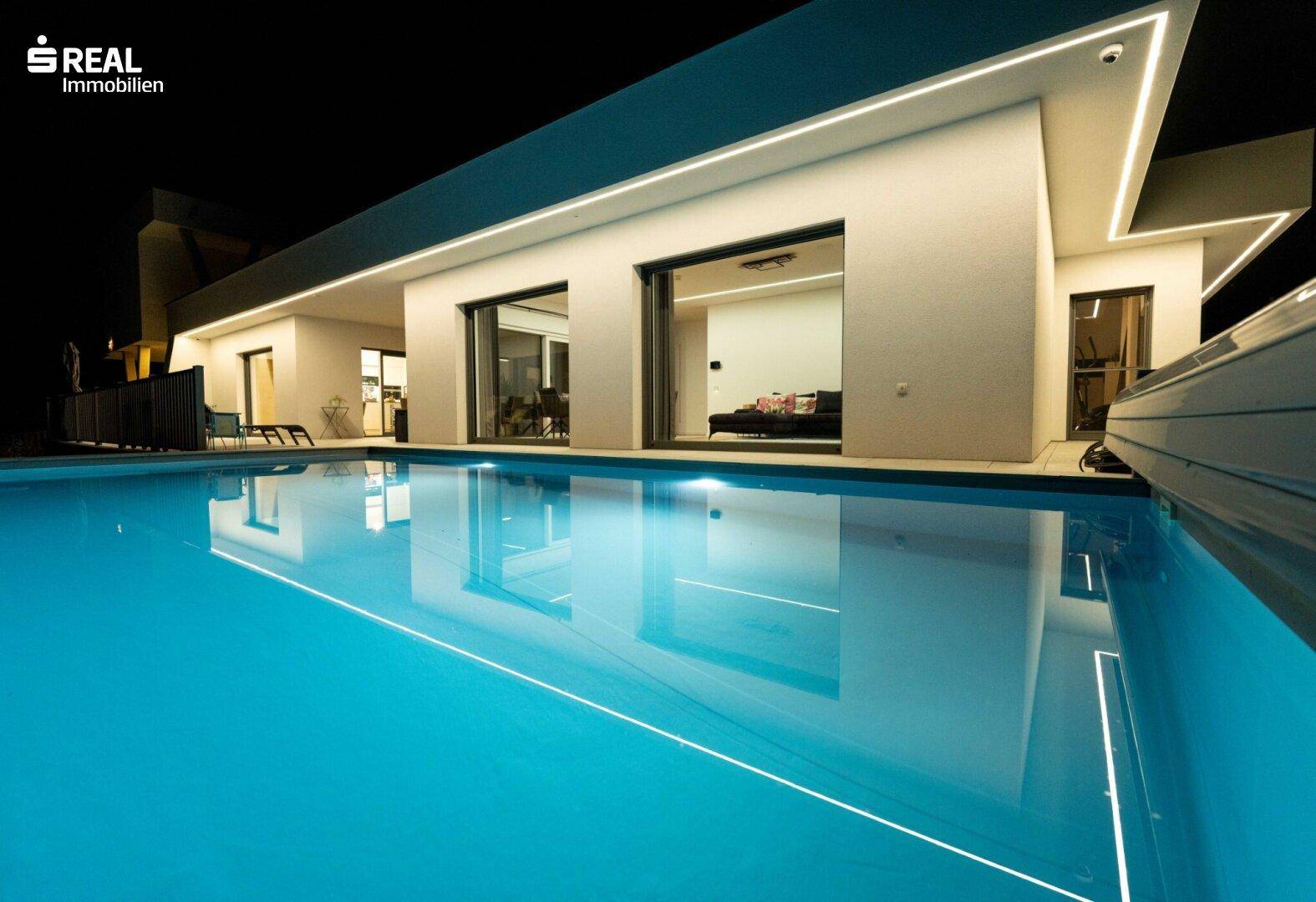 Moderne Villa bei Nacht mit beleuchtetem Pool und stilvoller Außenbeleuchtung.