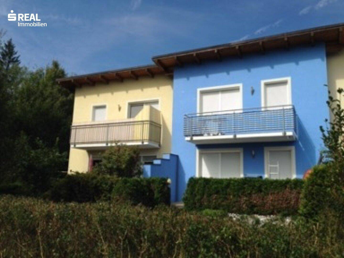 Ansicht der farbenfrohen Fassade eines Mehrfamilienhauses mit mehreren Balkonen unter blauem Himmel.