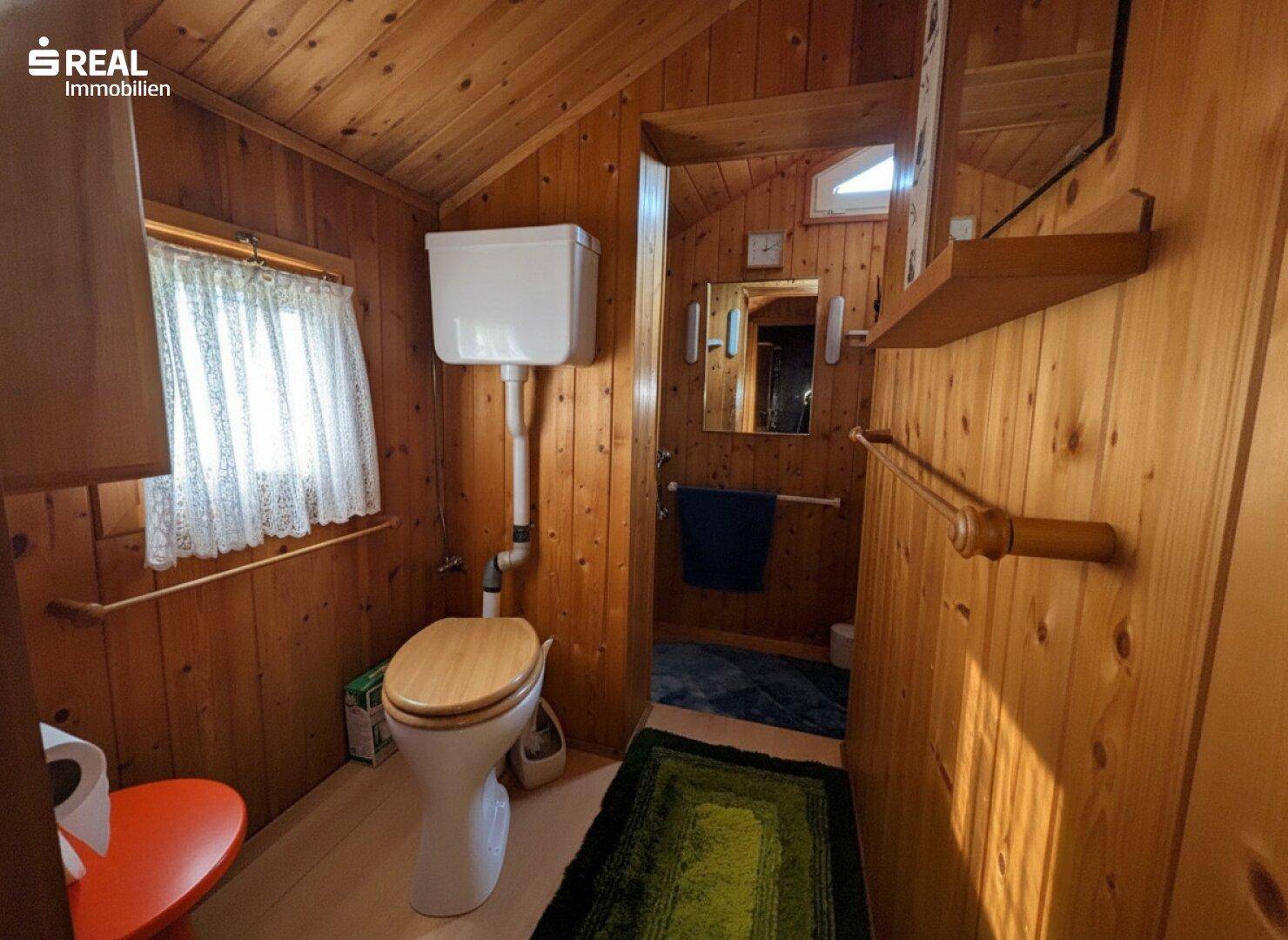 Rustikales Badezimmer mit Holztäfelung, Toilette und einem kleinen Fenster für natürliches Licht.