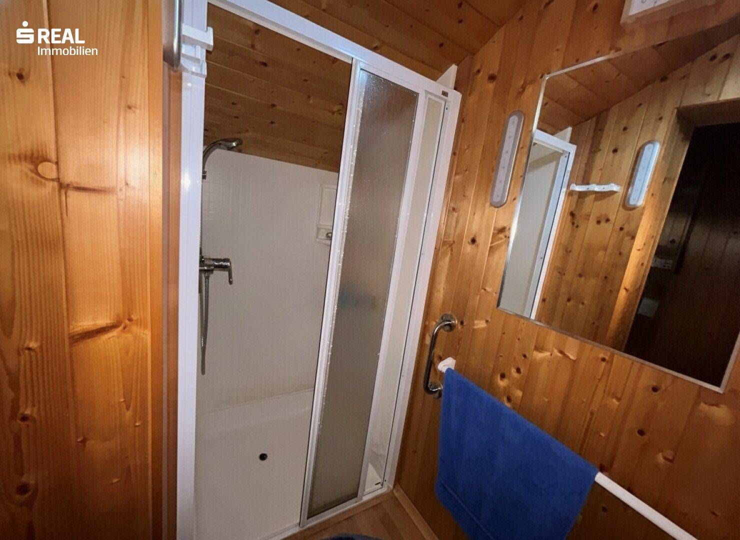 Duschbereich in einem holzgetäfelten Badezimmer mit Duschkabine und Handtuchhalter.