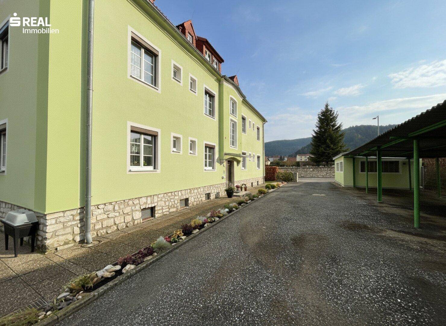 Seitenansicht des Gebäudes mit Parkplätzen, Carport und Blick auf die umliegende Landschaft.