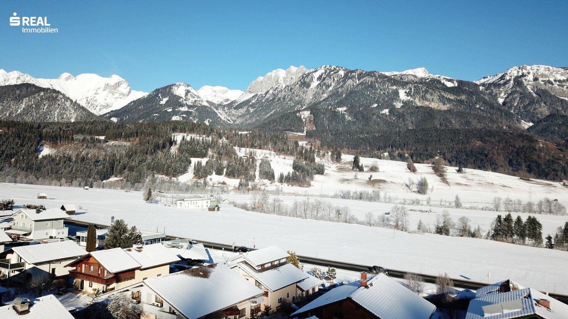 Winterliche Landschaft mit verschneiten Häusern und majestätischen Bergen im Hintergrund.
