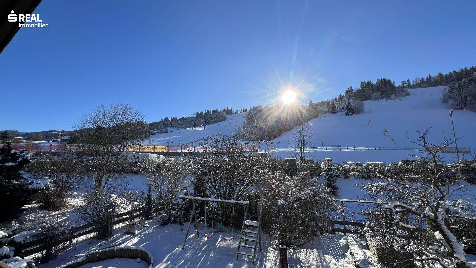 Verschneiter Garten mit Schaukel und Blick auf die winterliche Skipiste.