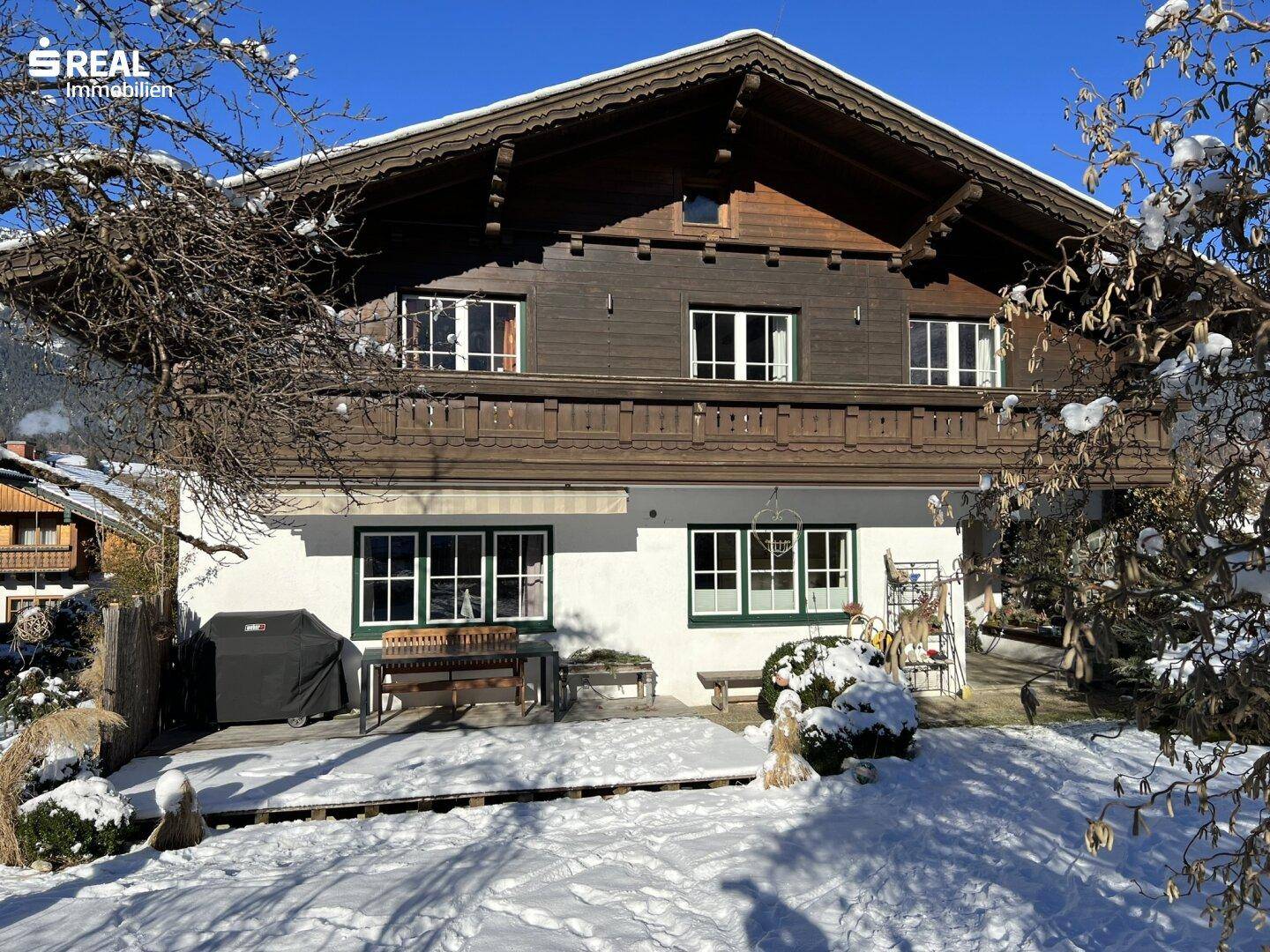 Traditionelles Haus im Winter mit verschneiter Terrasse und Garten.