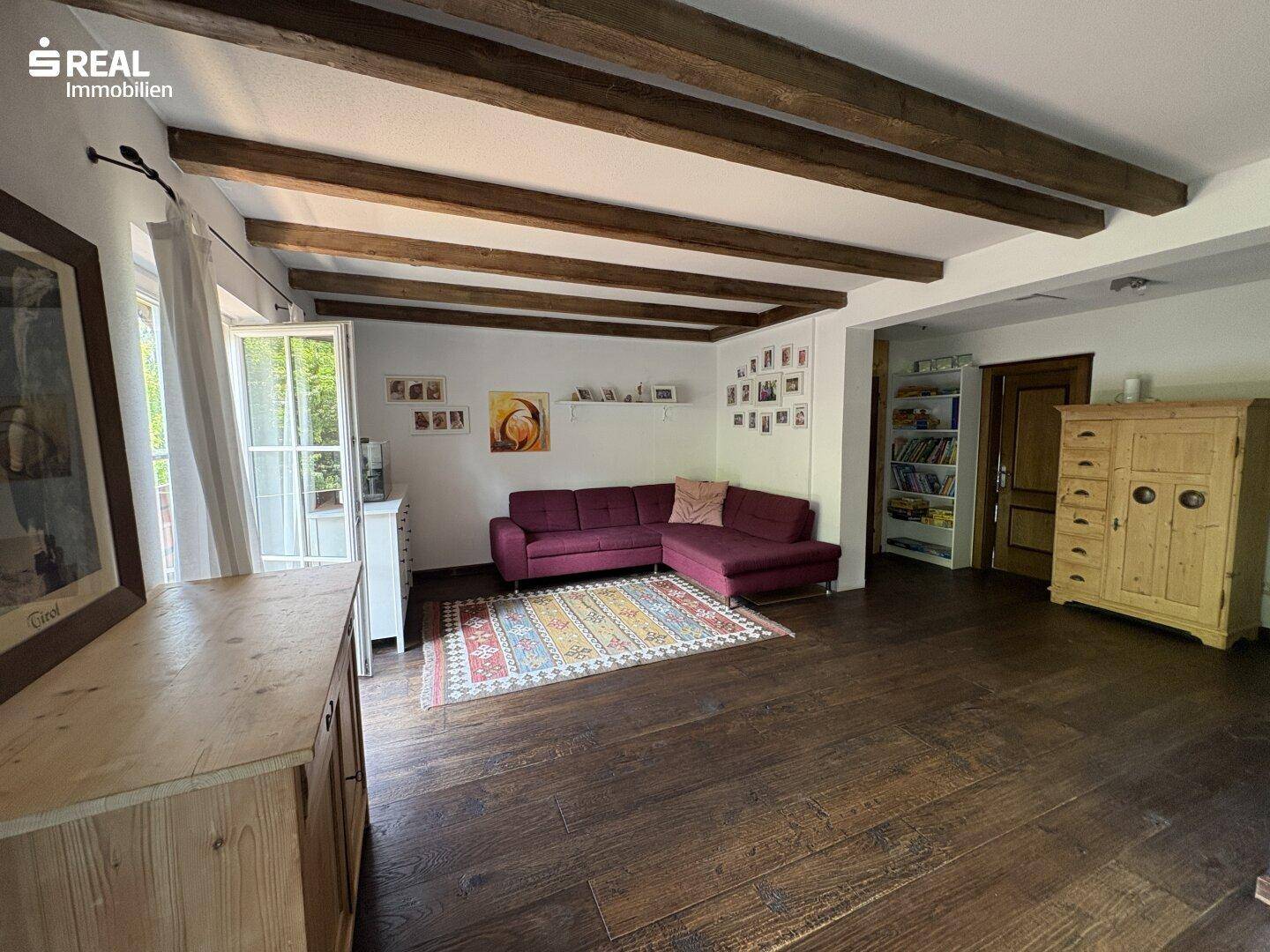 Geräumiges Wohnzimmer mit sichtbaren Holzbalken, dunklem Holzboden und gemütlichem Sofa.