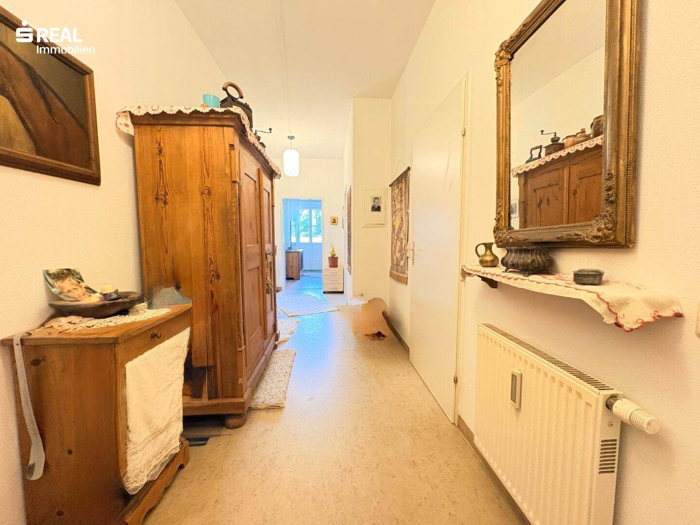 Langer Flur mit traditionellen Holzmöbeln, einem Spiegel und einem Heizkörper an der Wand.