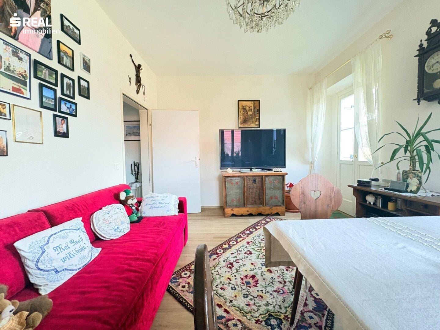 Gemütliches Wohnzimmer mit rotem Sofa, Fernseher und traditionellen Dekorationselementen.