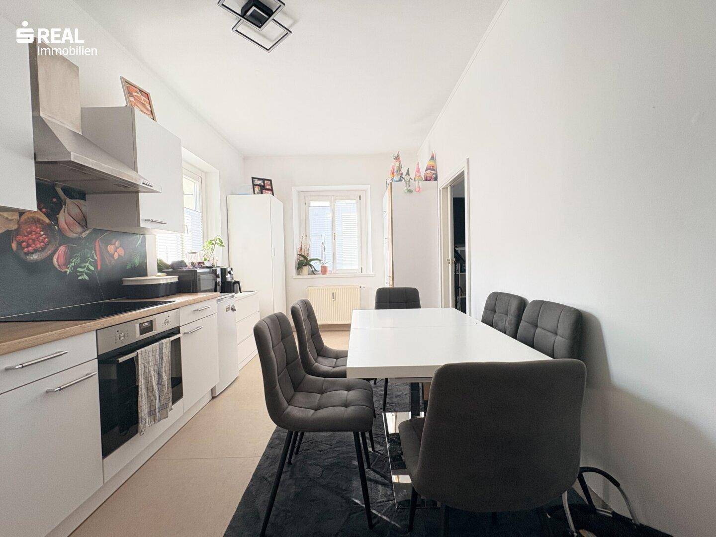 Moderne Küche mit weißer Einbauküche, Essbereich und Fenster für natürliches Licht.
