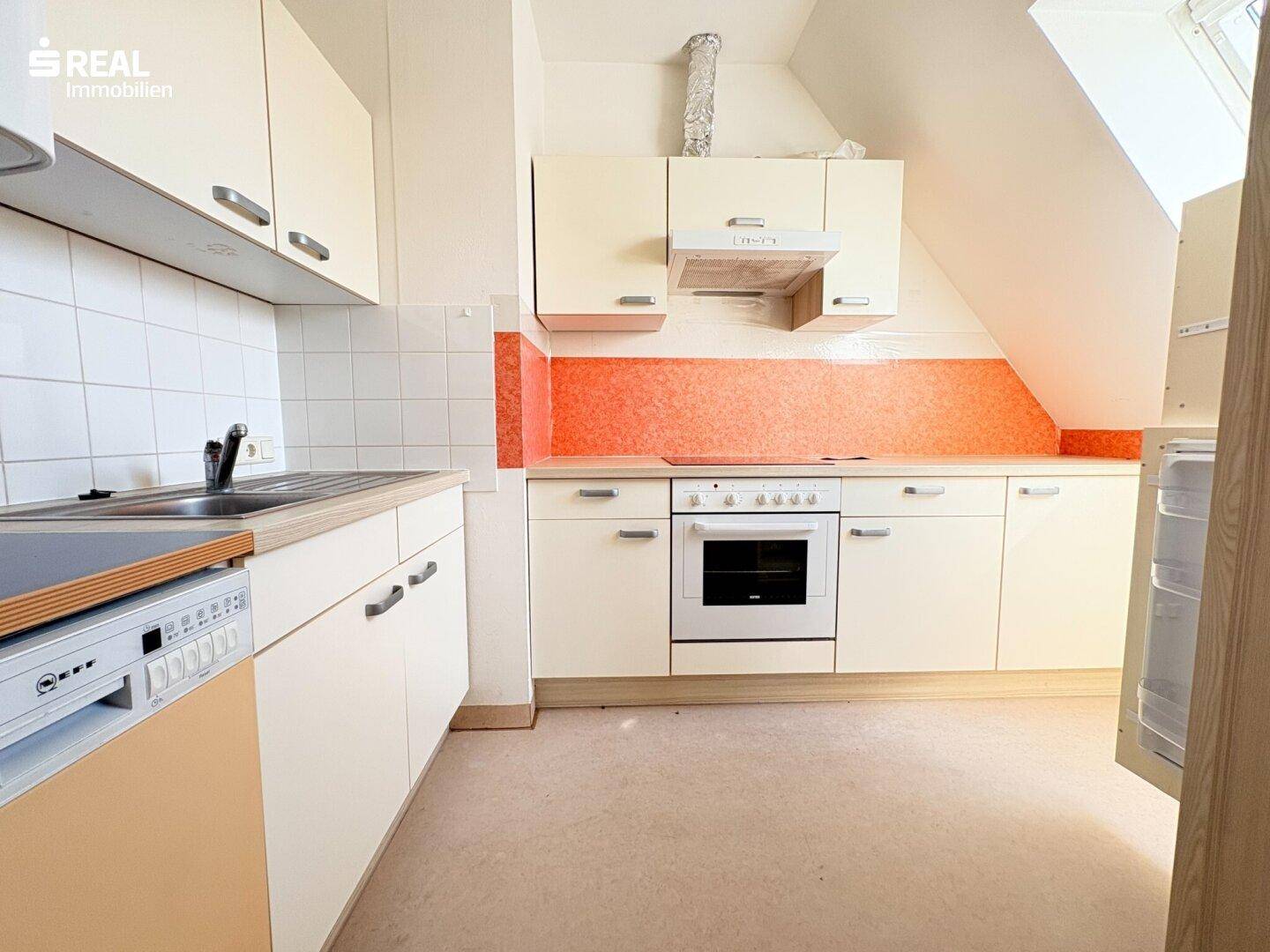 Helle Küche mit cremefarbenen Schränken, orangefarbenem Fliesenspiegel und Dachschräge.