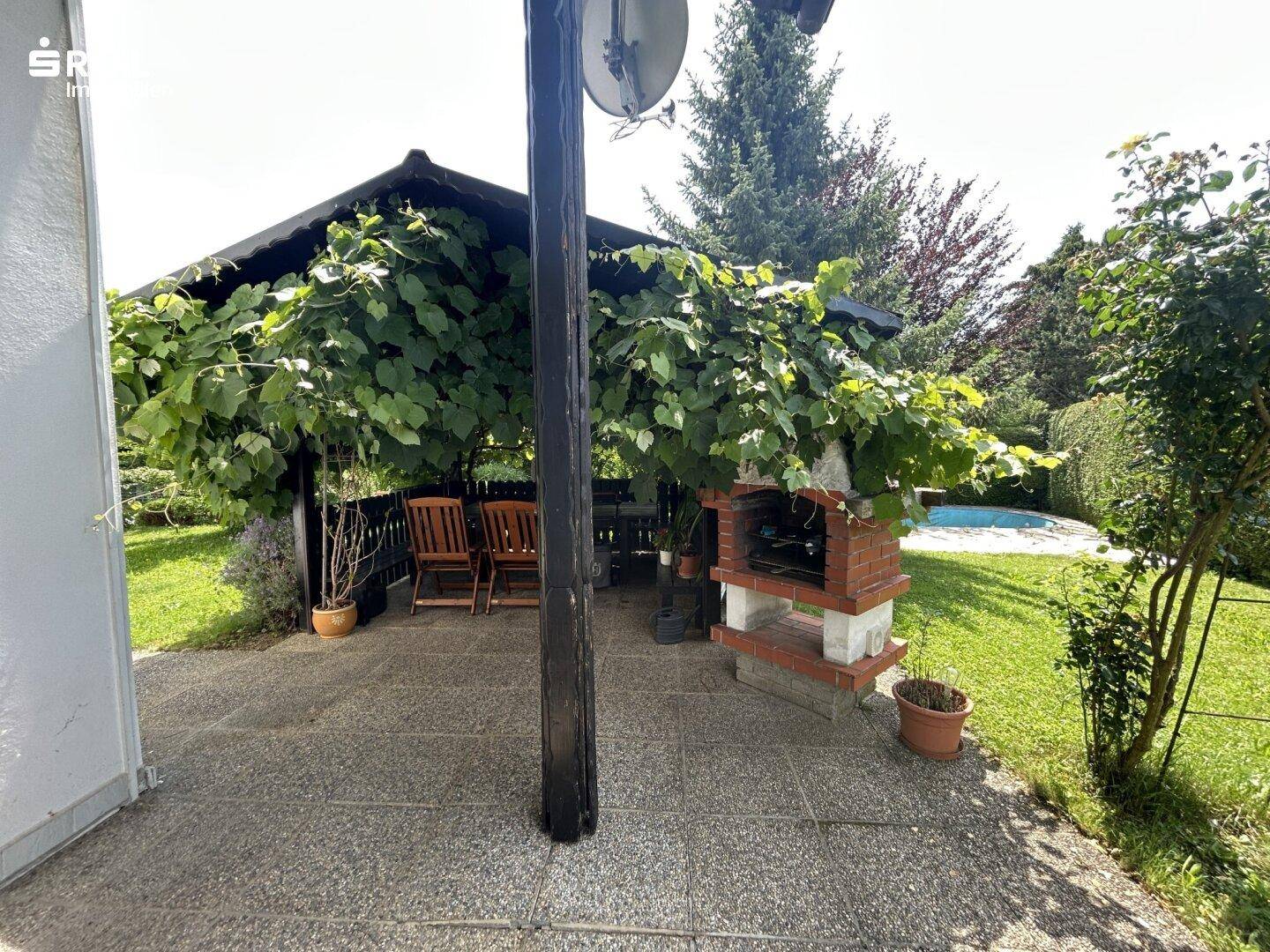 Gemütlicher überdachter Sitzbereich im Freien mit Grill und Blick auf den Pool im Garten.