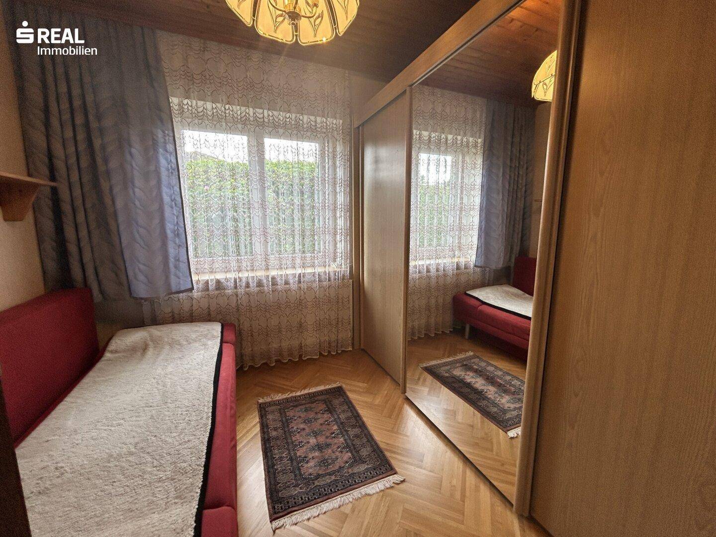 Gemütliches Zimmer mit Holzdecke, Parkettboden und einem großen Spiegelschrank, ideal als Gästezimmer.