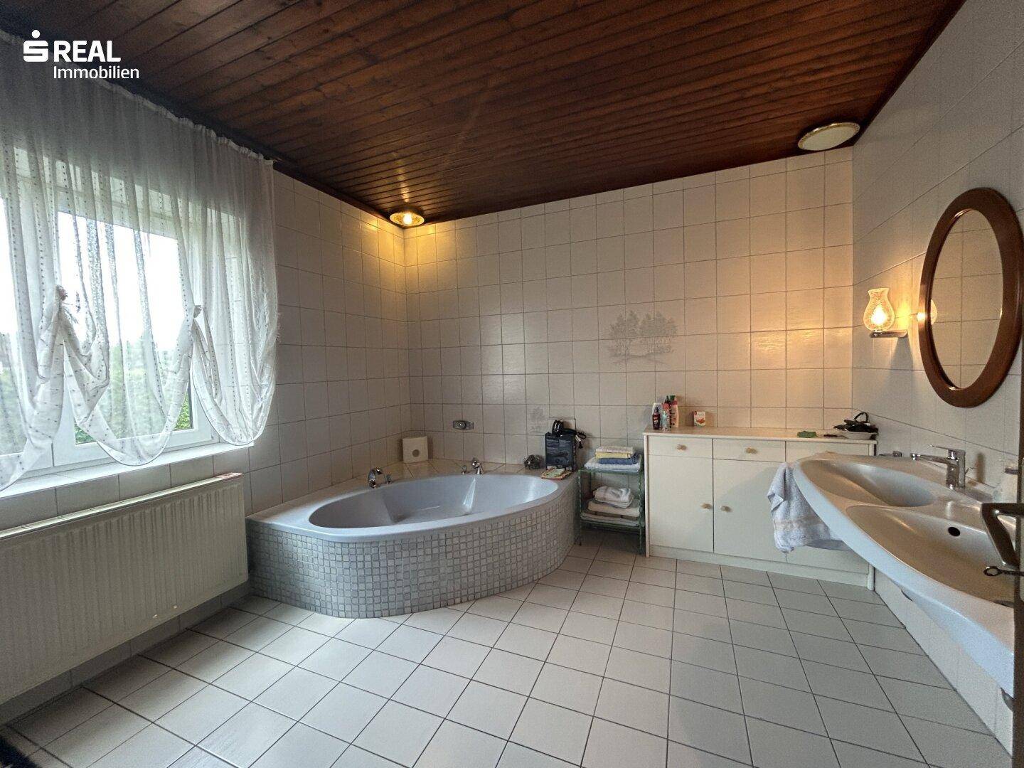 Geräumiges Badezimmer mit Eckbadewanne, Doppelwaschbecken, weißen Fliesen und Holzdecke.