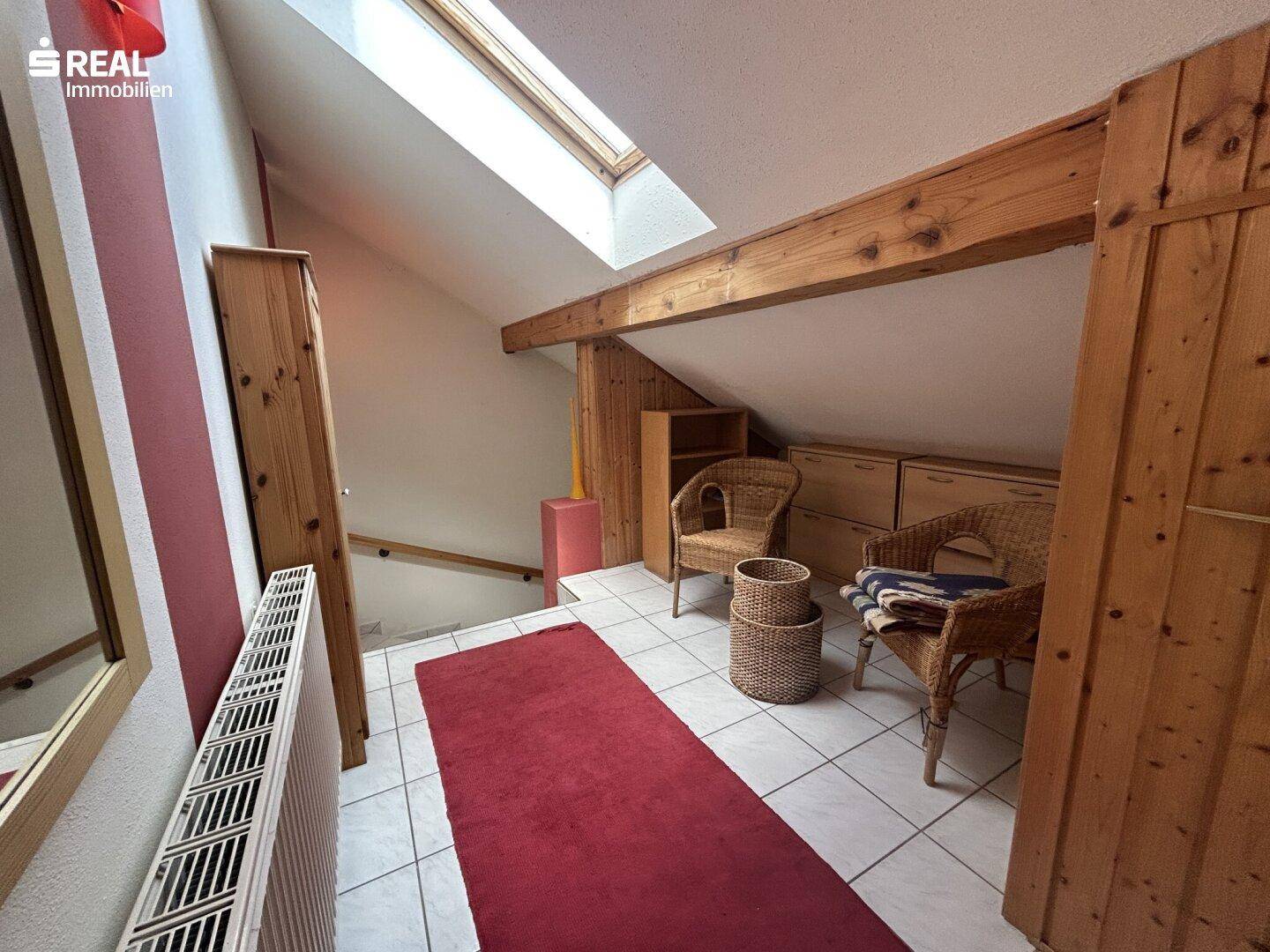 Heller Flurbereich im Dachgeschoss mit Dachfenster, sichtbaren Holzbalken und Fliesenboden.