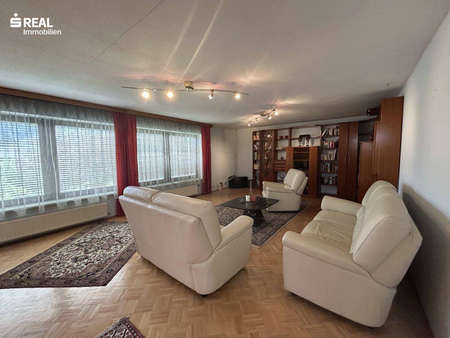 Geräumiges Wohnzimmer mit Parkettboden, bequemen Ledersofas und einem Bücherregal an der Wand.