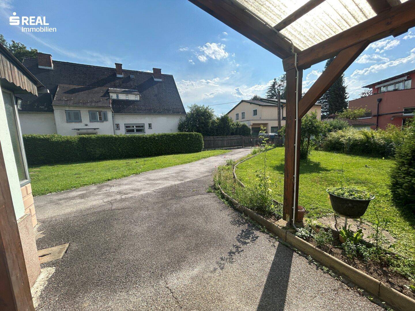 Blick vom überdachten Bereich über die Einfahrt zum weitläufigen Garten und Nachbargebäuden.